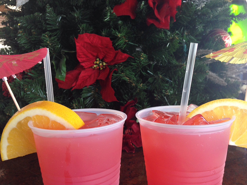 Two cups with a pink drink in front of a holiday decoration